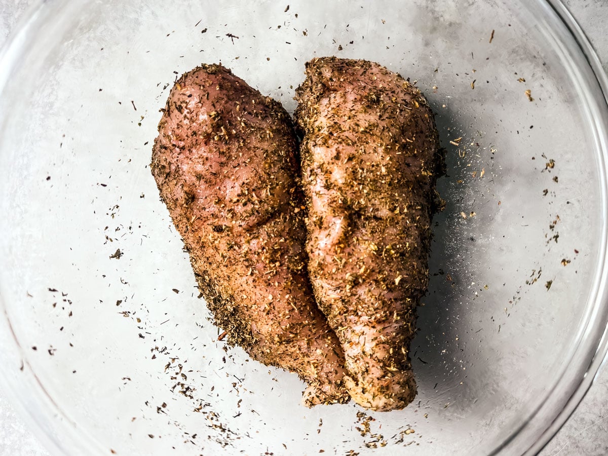 Seasoned chicken breasts in a mixing bowl.