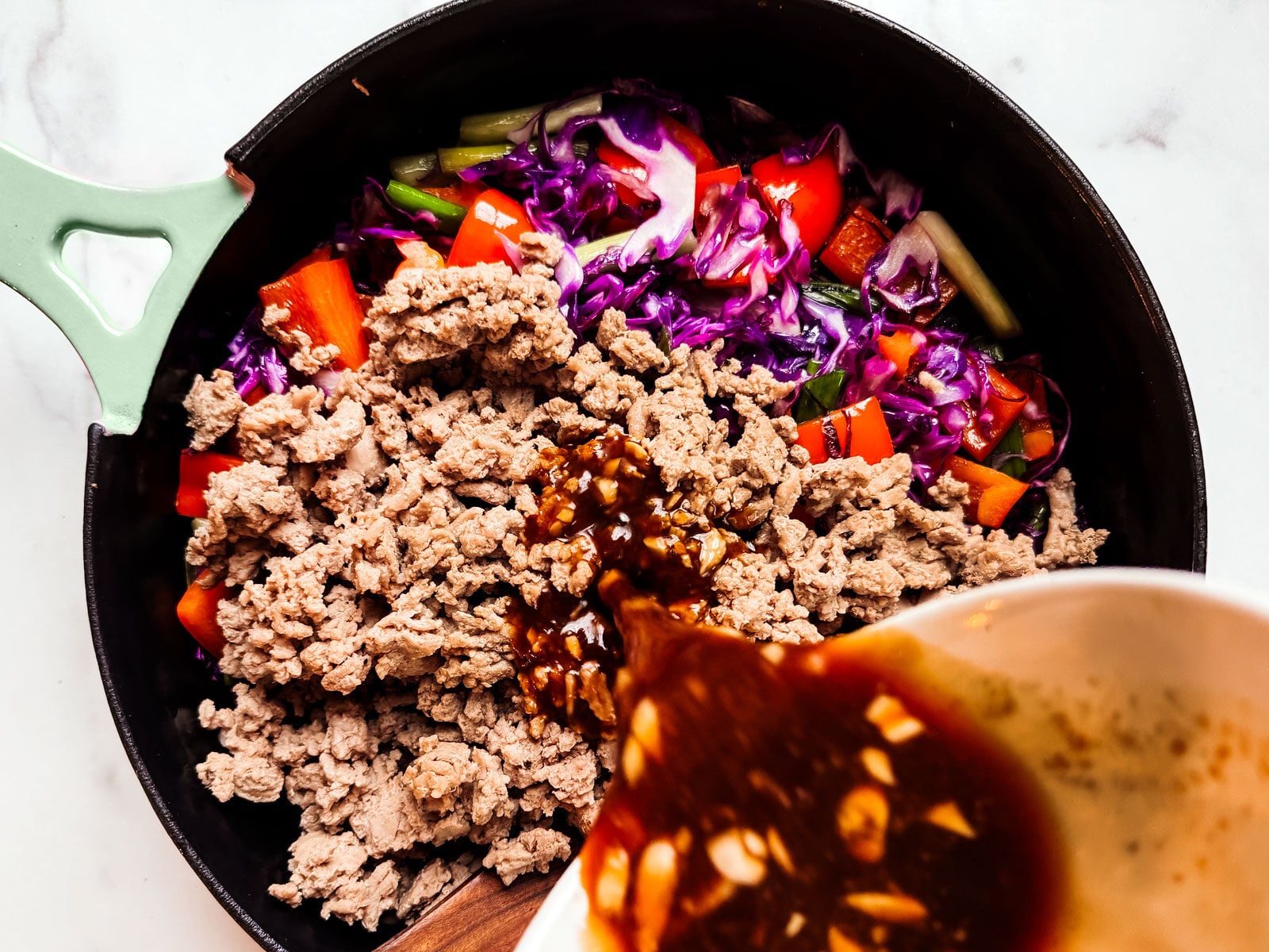 Ground turkey and vegetables in a skillet with sauce being poured over it.
