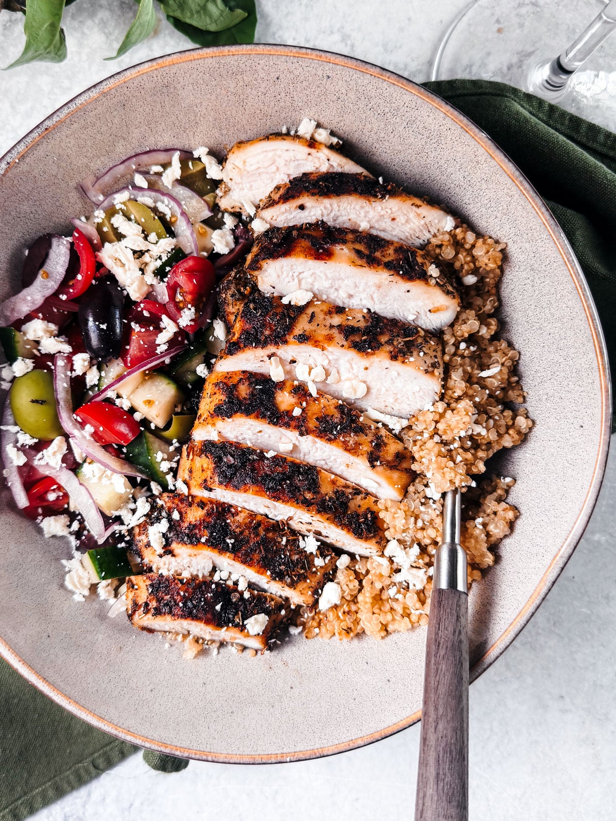Bowl of quinoa topped with grilled sliced chicken, fresh veggies, and tzazizki.