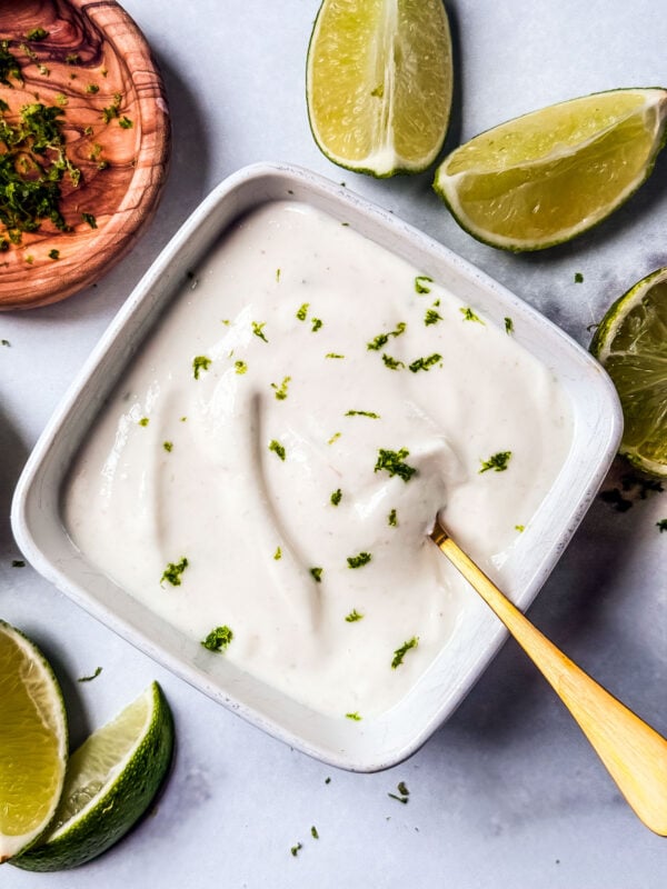 greek yogurt lime crema in a bowl surrounded by limes.