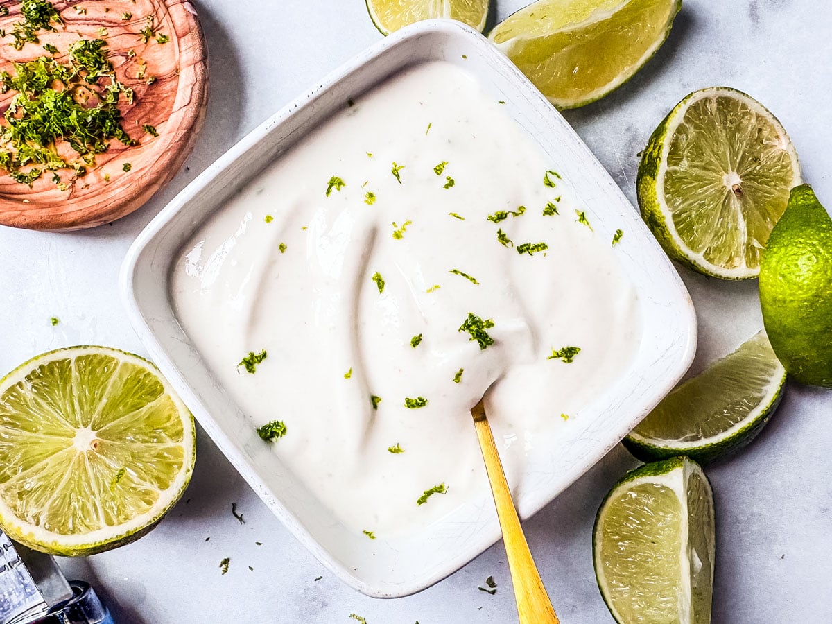 lime crema in a small bowl surrounded by limes.