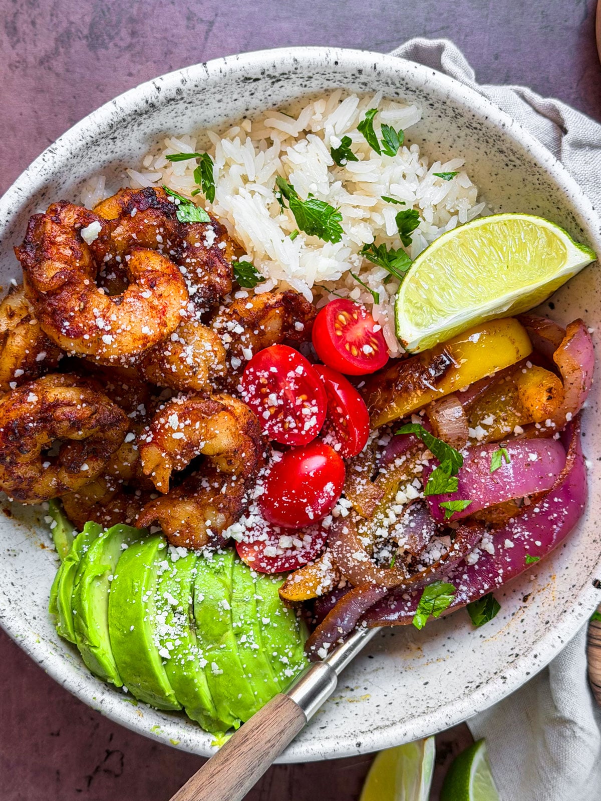 Bowl of seasoned shrimp, rice, and veggies with cheese and avocado.