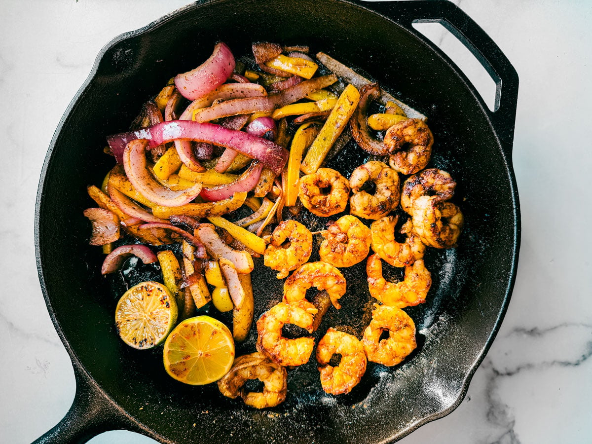 Shrimp, peppers, onions, and charred limes in a cast-iron skillet.